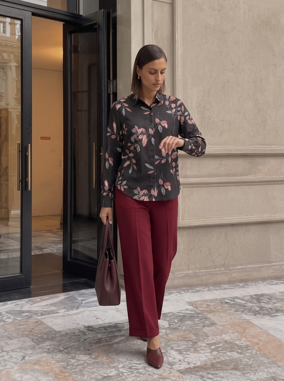 Woman wearing a black long-sleeve floral print button-down shirt tucked into burgundy trousers