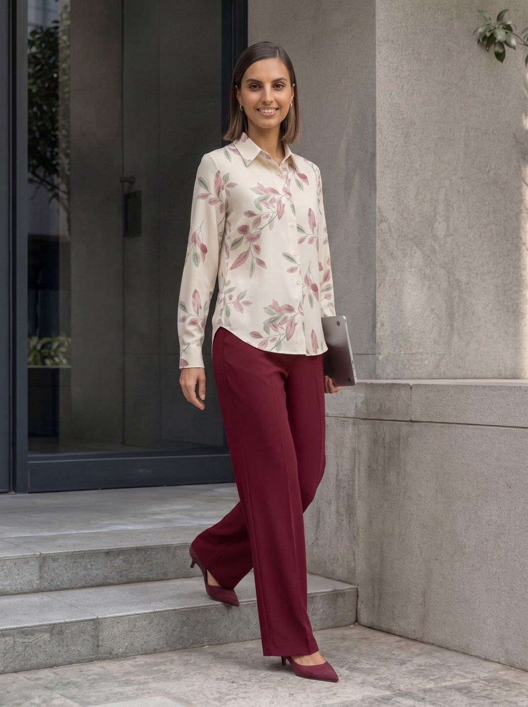 Woman wearing a cream botanical print long-sleeve collared shirt with burgundy trousers