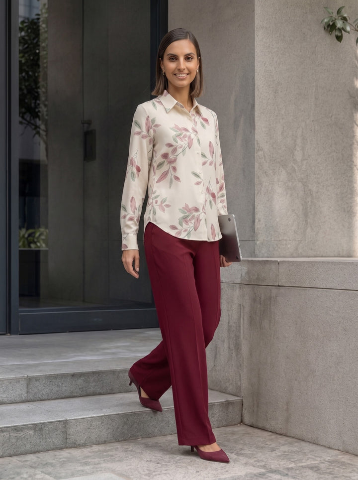 Woman wearing a cream botanical print long-sleeve collared shirt with burgundy trousers